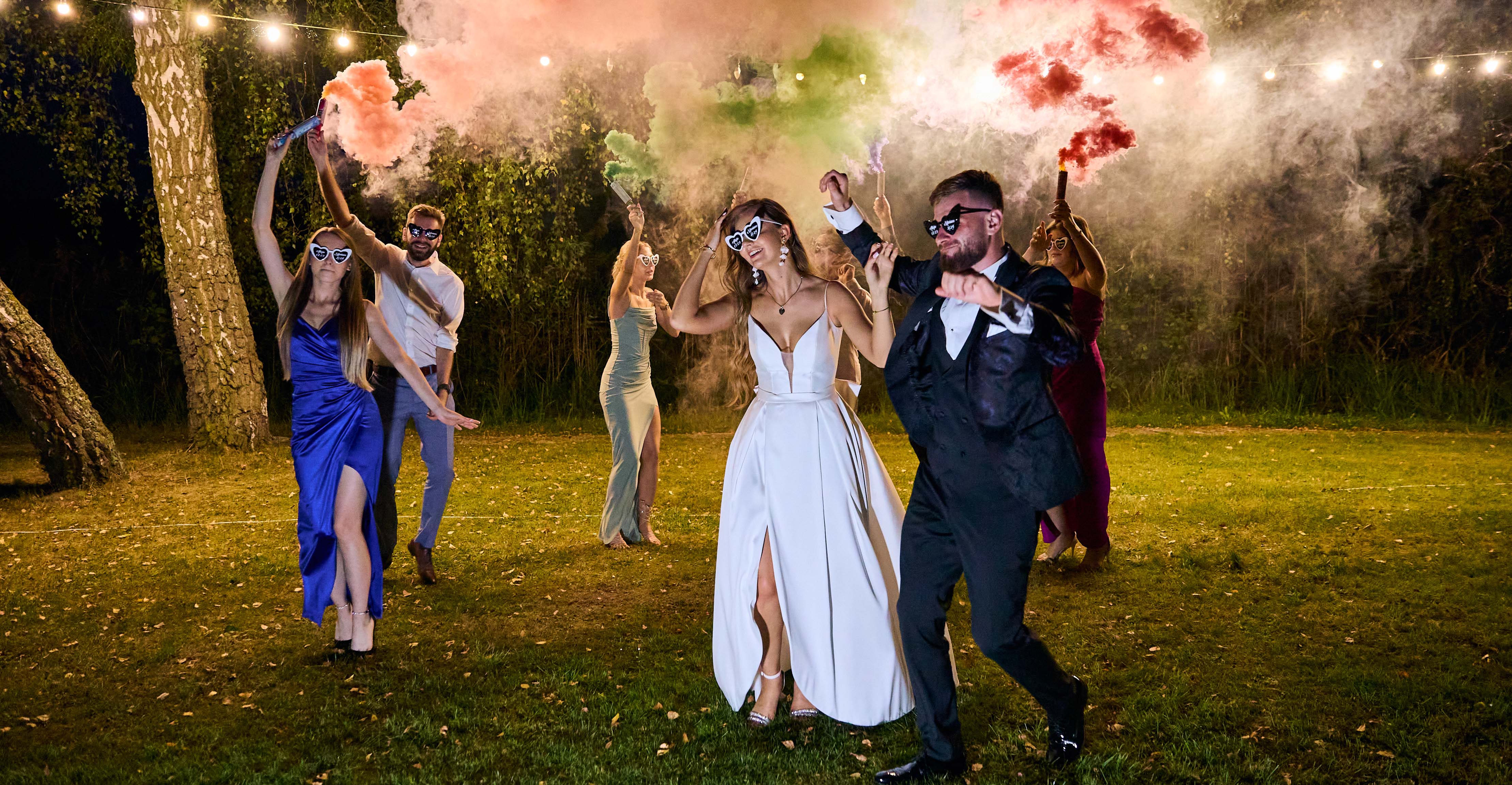 Chwile pełne szczęścia i radości. Para łoda w towarzystwie swoich przyjaciół podczas zabawy z racami dymnymi.